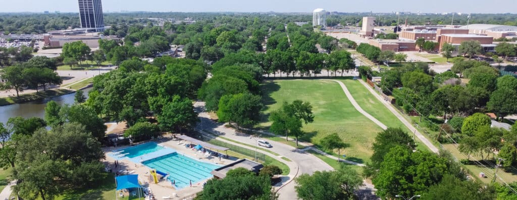 Aerial view communityinfrastructure near downtown Richardson, Texas, USA. Green park surrounded by trails, local pond and busy outdoor parking lots