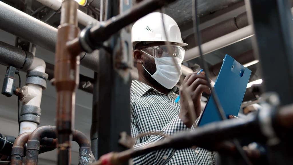 Worker wearing safety gear documenting observations as part of a Safety assessment in an industrial setting.