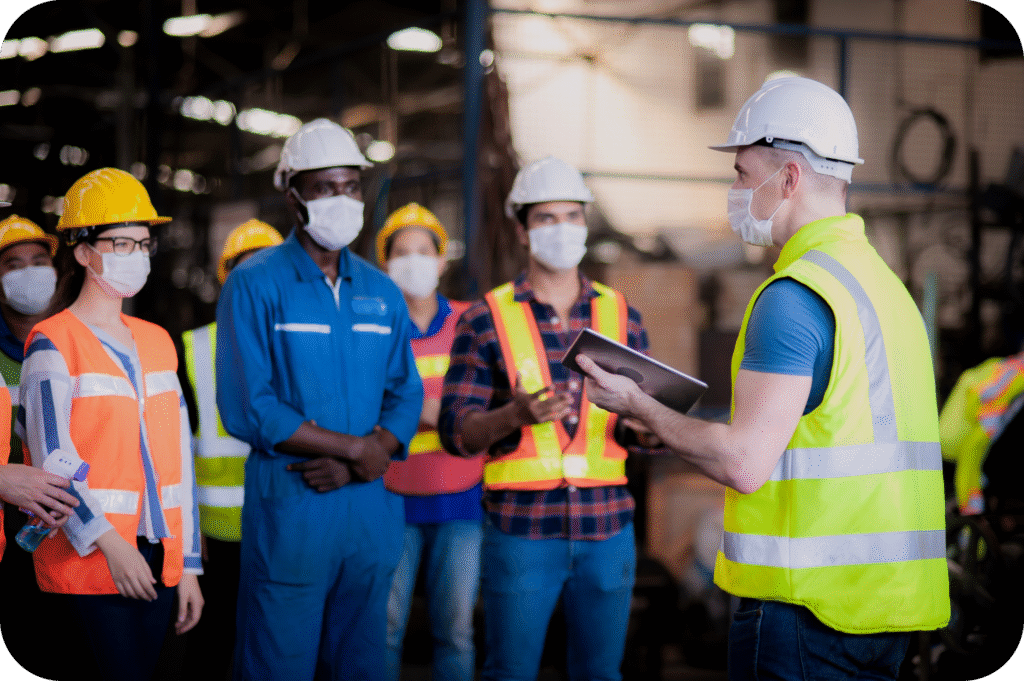 Construction supervisor leading toolbox talk with team using digital tablet on factory floor.