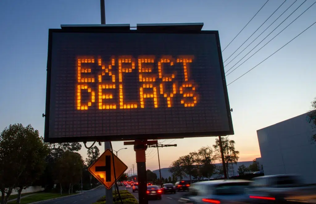Portable message board displaying “EXPECT DELAYS” at dusk near a construction zone.
