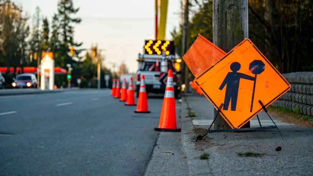 Roadside work zone with orange cones and a flagger warning sign beside a utility truck.