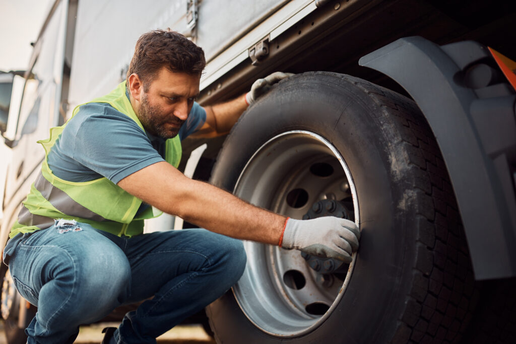 A commercial truck driver inspecting a truck tire during a pre-trip check.
