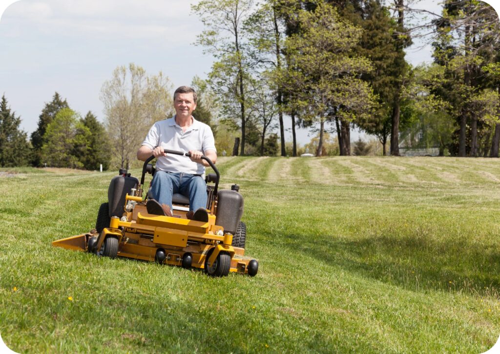 Man operating a ride-on lawnmower on a grassy field during outdoor mowing work.
