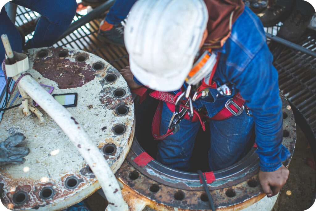 A confined space worker conducts maintenance inside an industrial vessel, following confined space standards.