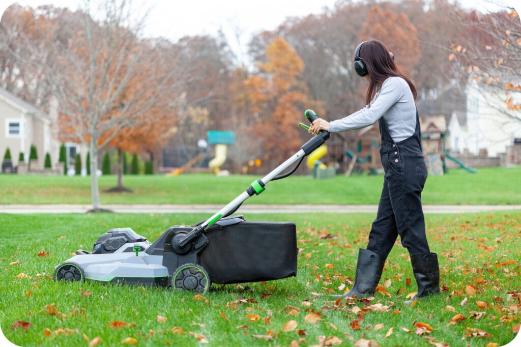 Person pushing a walk-behind lawnmower while wearing hearing protection in a residential outdoor area.