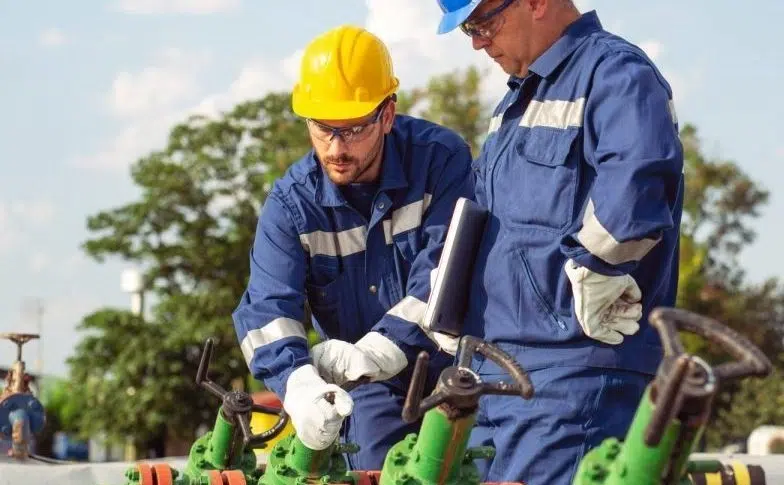 Two workers in hard hats perform hands‑on valve training during a coaching session.